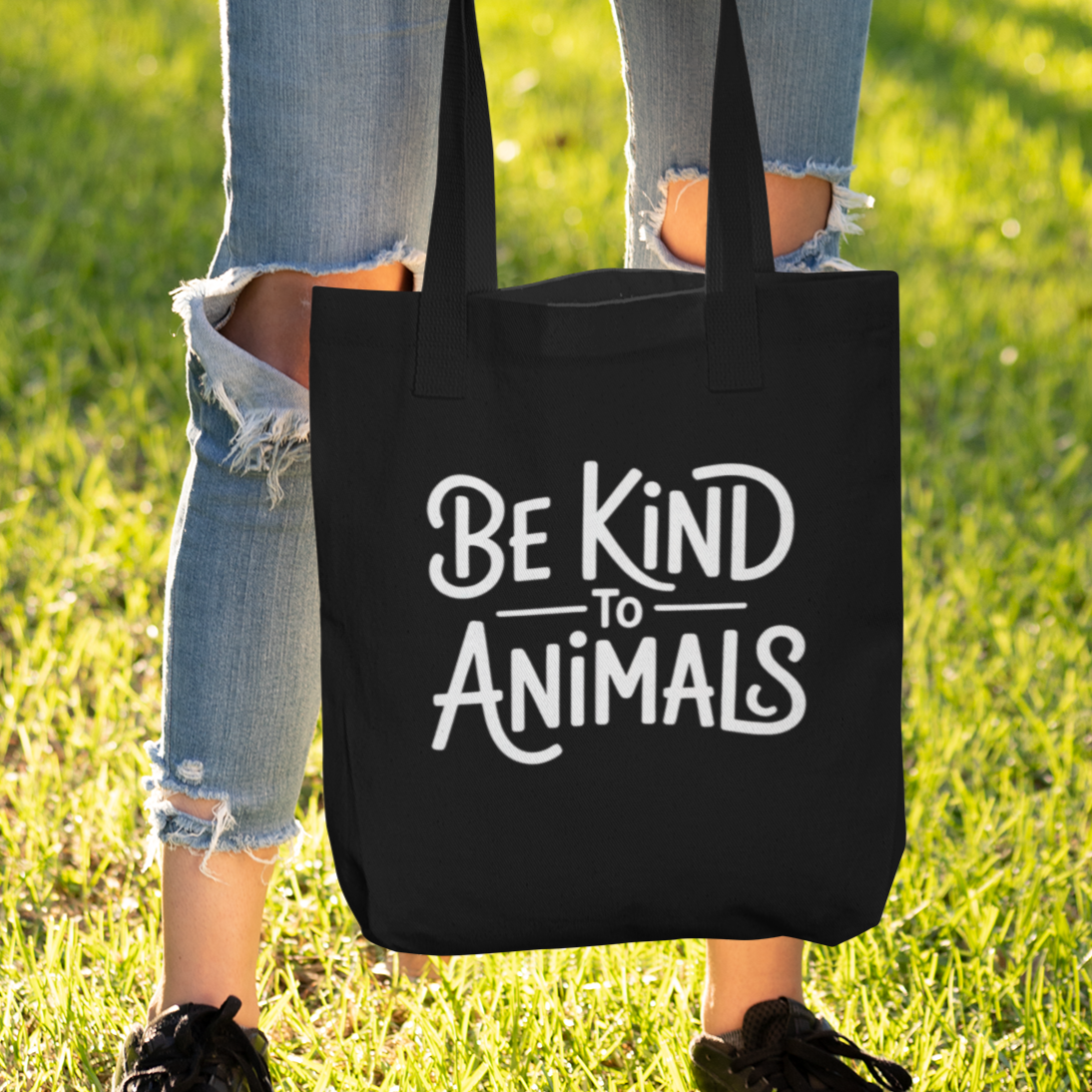 Woman holding a black animal rights tote bag with the slogan 'be kind to animals'