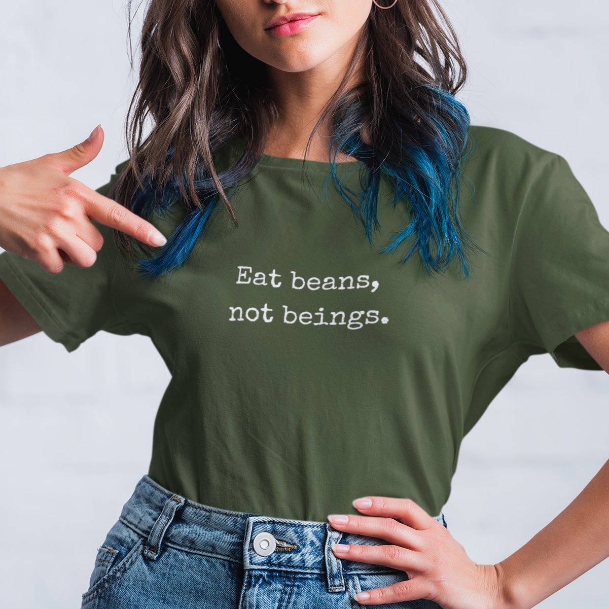 Woman wearing a funny khaki green minimalist vegan t-shirt with the slogan 'eat beans not beings'.