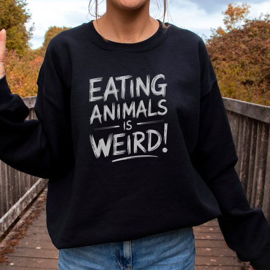 woman standing on a bridge wearing a black sweatshirt with the slogan 'eating animals is weird'