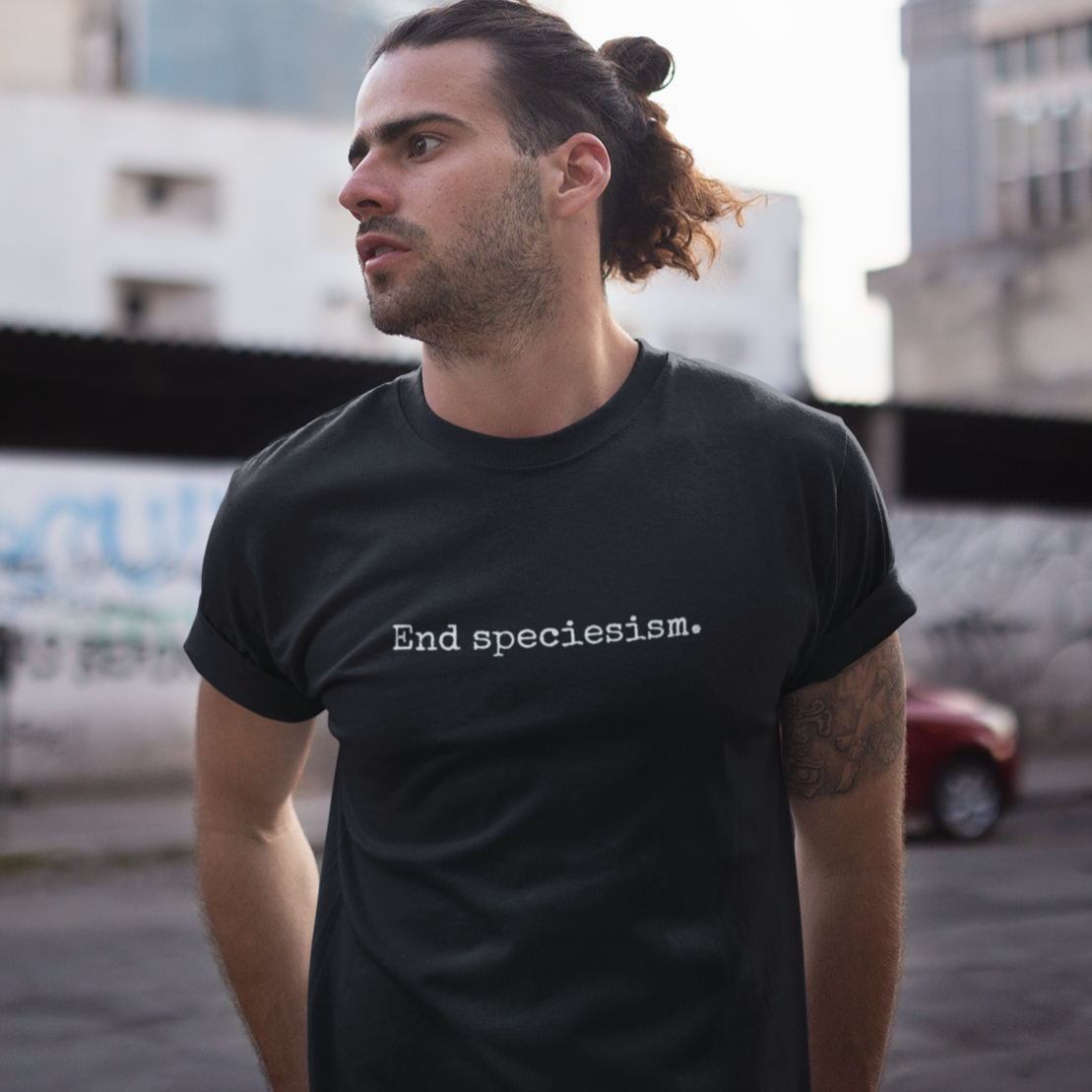Man wearing a minimalist vegan t-shirt with the animal rights slogan 'end speciesism' in a small typewriter font.