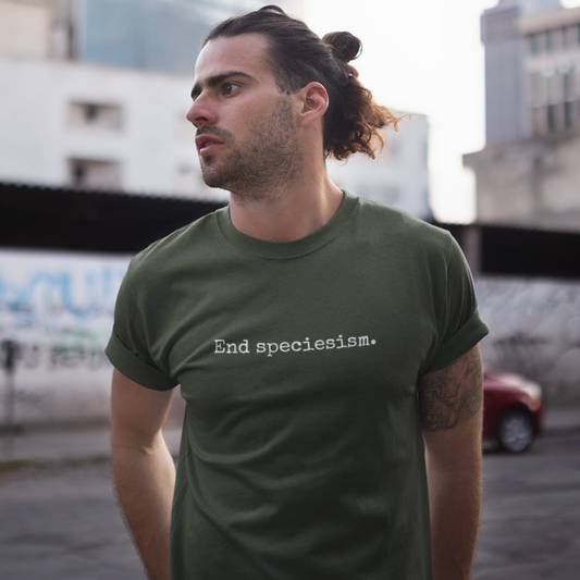 Man wearing a khaki green minimalist animal rights t-shirt with the slogan 'end speciesism' written in small writing in a typewriter font.
