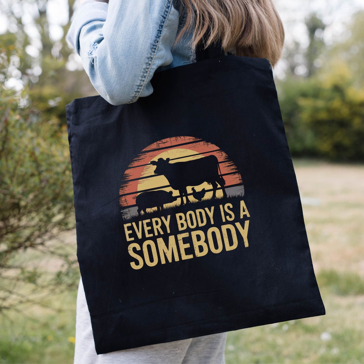 Black vegan tote bag with a graphic
 of farm animals and a sunset, and the slogan 'Every Body Is A Somebody'
