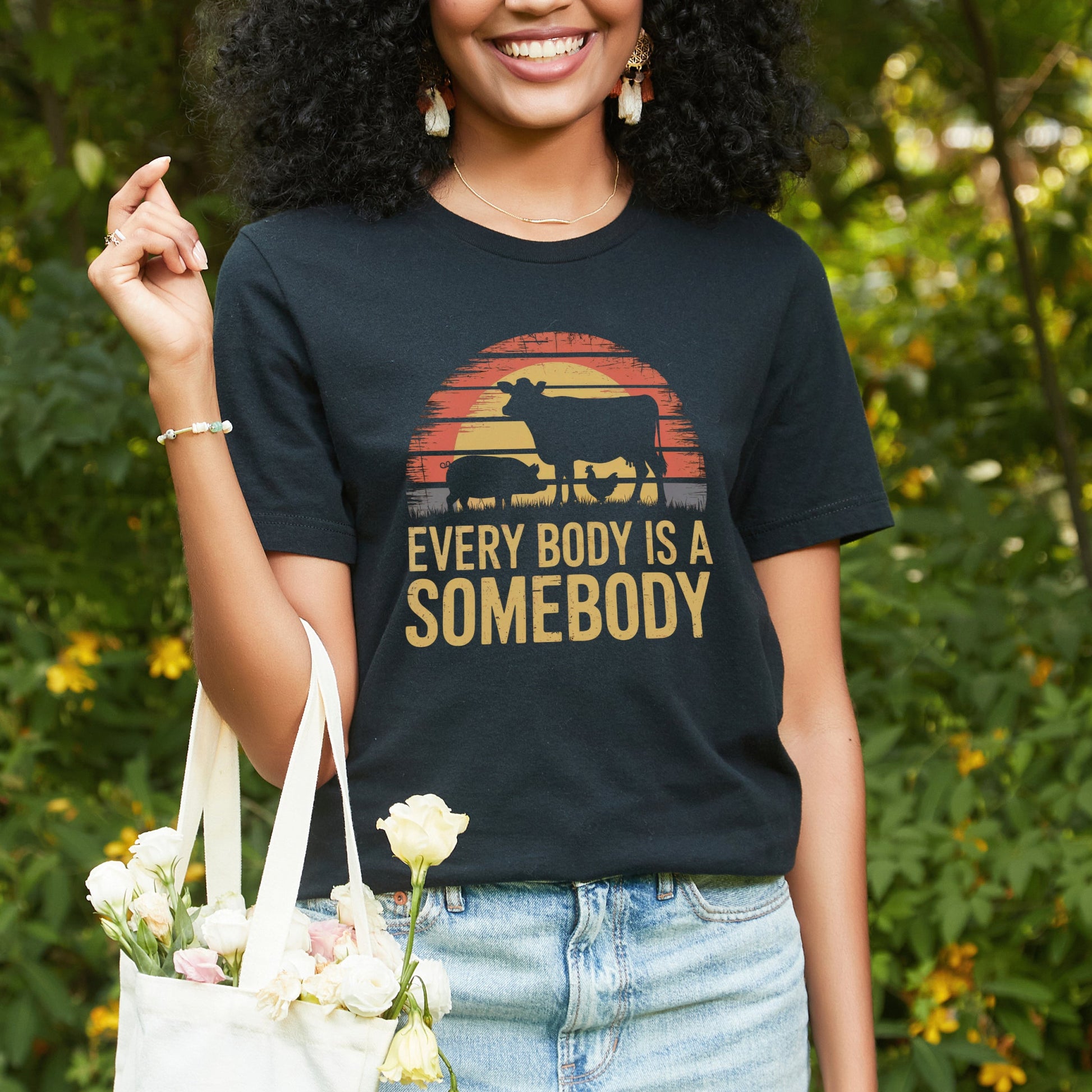 Black vegan or vegetarian t-shirt with a picture of a unset with farm animal silhouettes, and the slogan Every Body Is A Somebody.