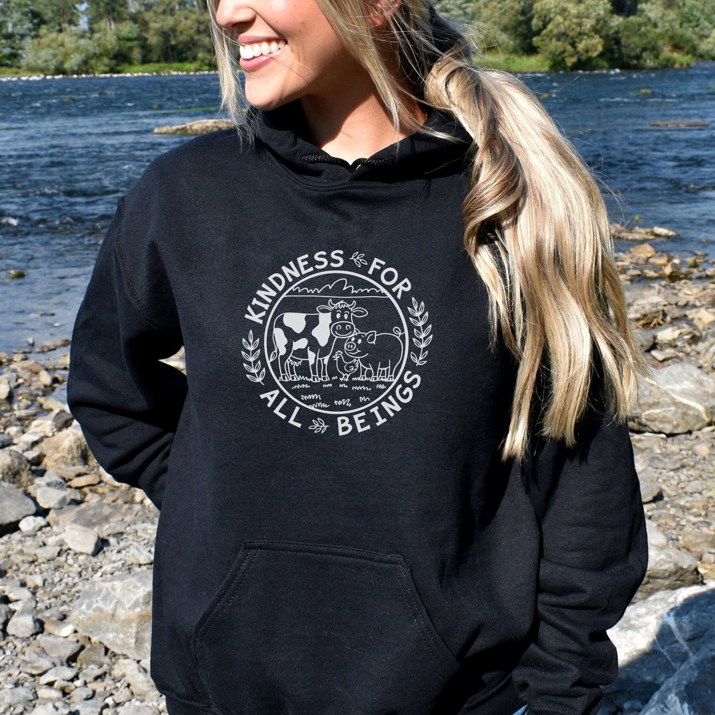 Woman wearing a black vegan hoodie with a circular design of farm animals and the slogan 'kindness for all beings' 