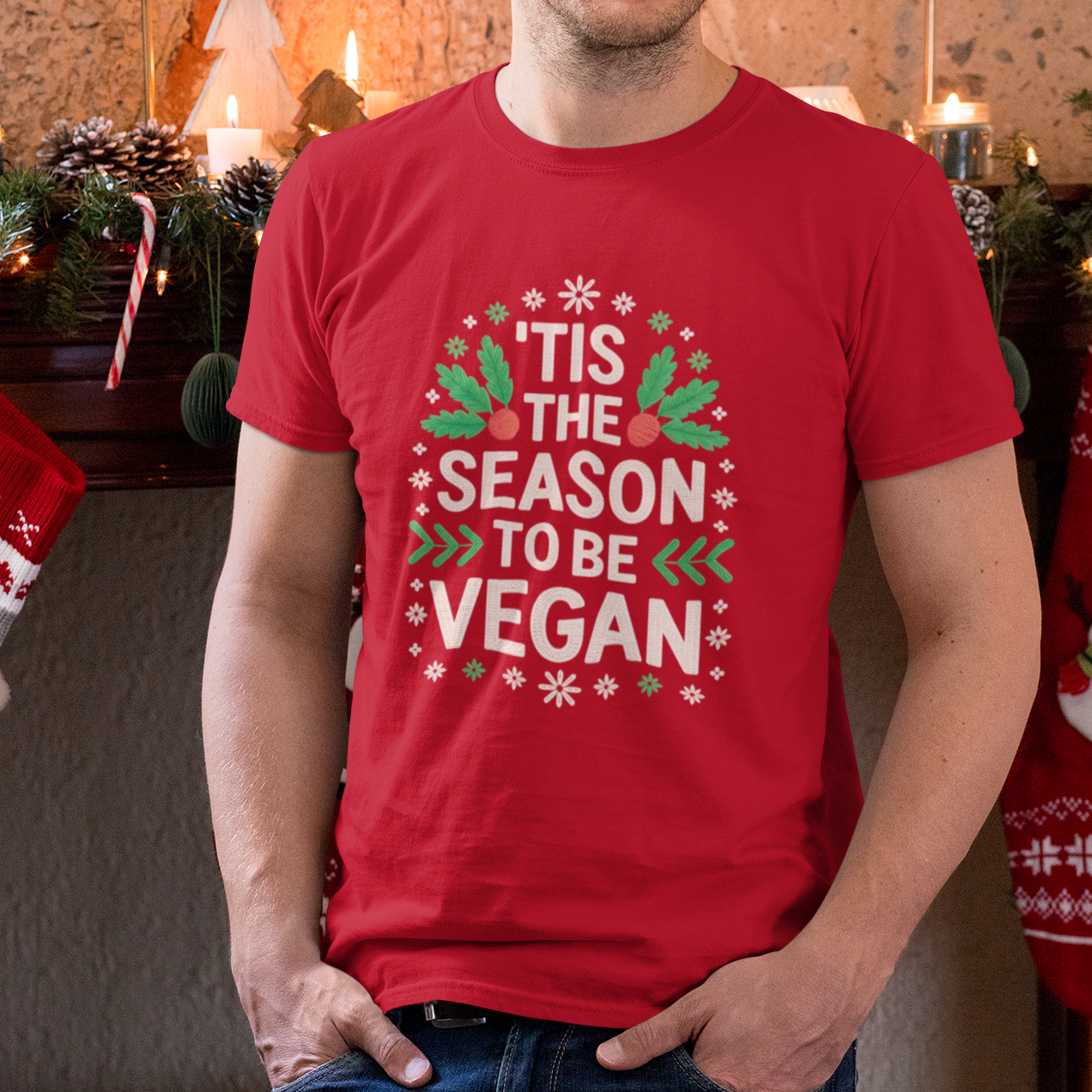 Man wearing a red t-shirt with 'Tis the Season to be Vegan text in a festive design, standing in a decorated room.
