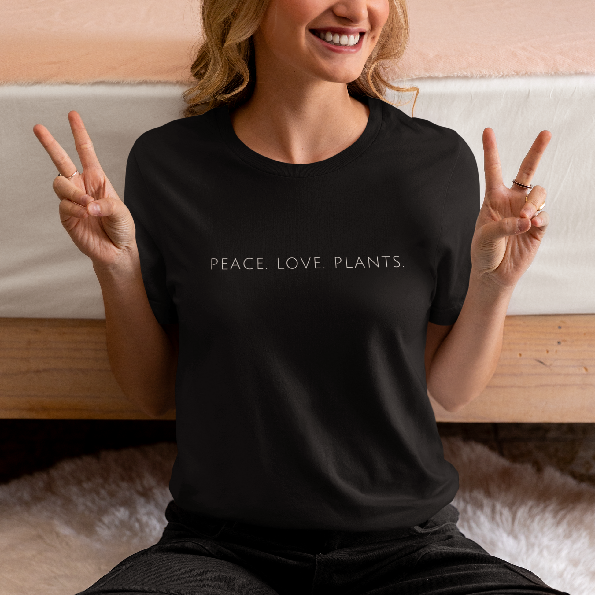 Woman wearing a black minimalist vegan t shirt with the slogan 'Peace. Love. Plants.'