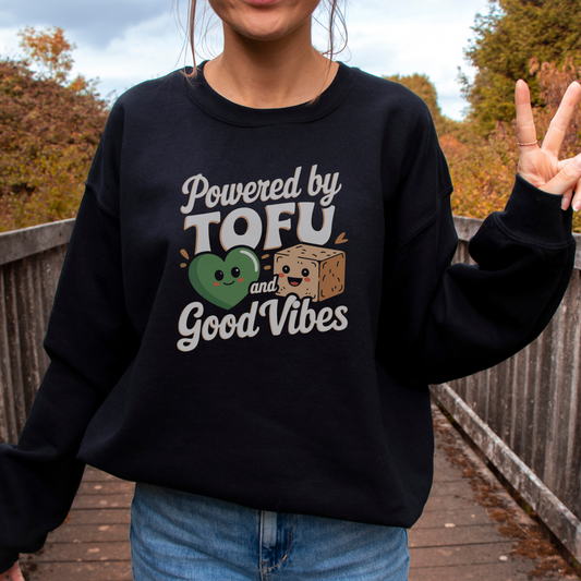 Woman standing on a wooden bridge giving the peace sign and wearing a black vegan sweatshirt with the slogan 'powered by tofu and good vibes'.