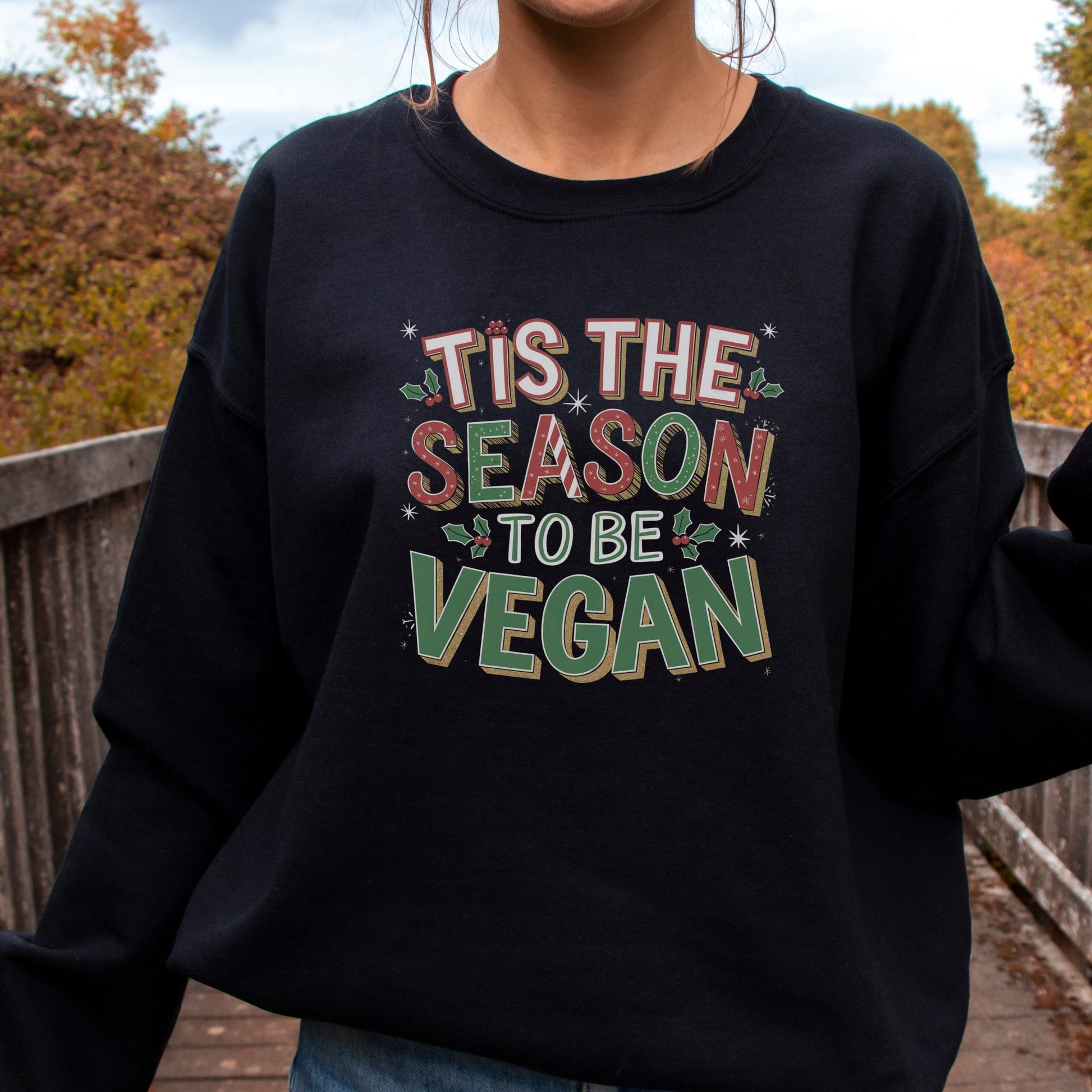 woman wearing a black vegan Christmas jumper with the slogan 'tis the season to go vegan' 