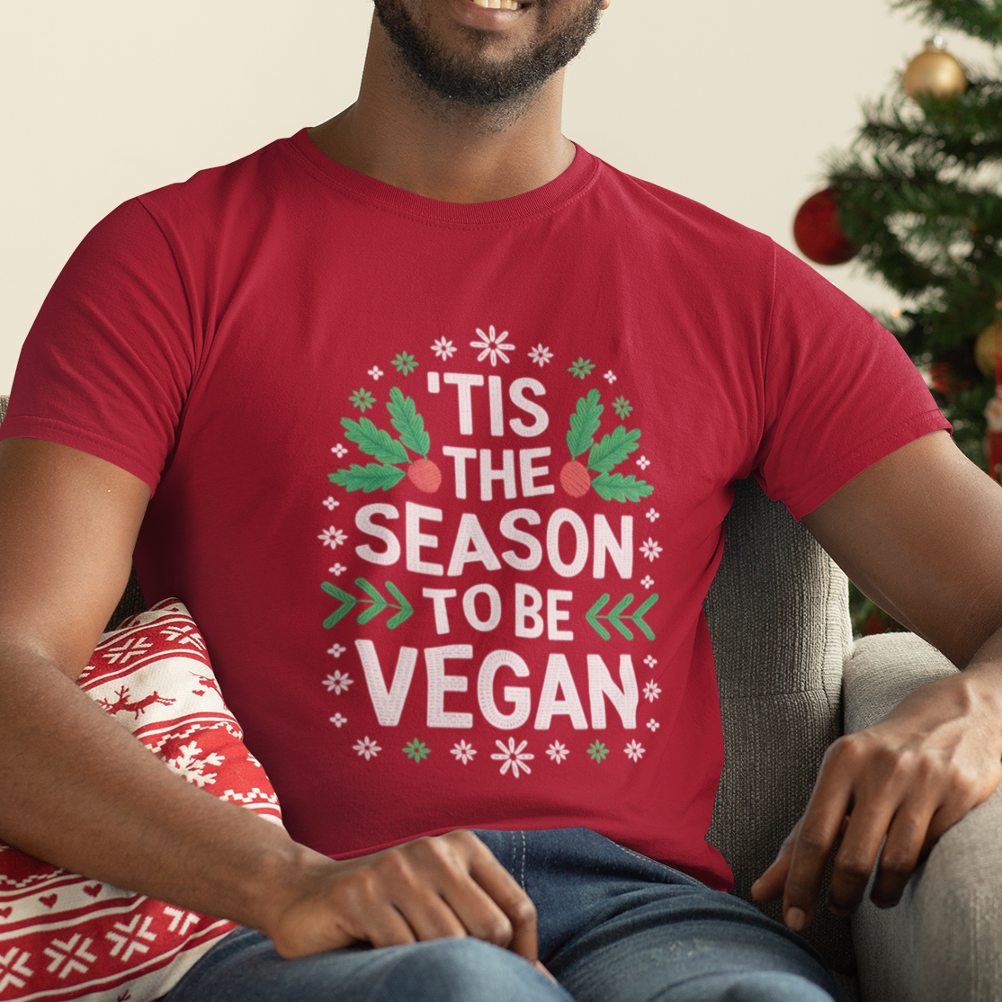 Man wearing a red 'Tis the Season to be Vegan' shirt sitting in front of a Christmas tree.