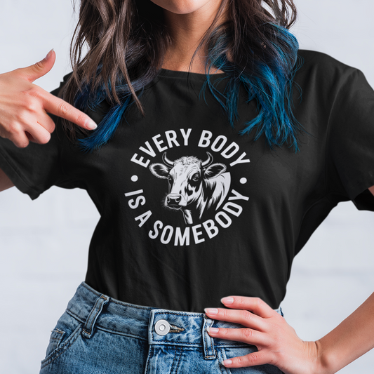 Person wearing a black vegan t-shirt with the slogan 'every body is a someody' and a picture of a cow.